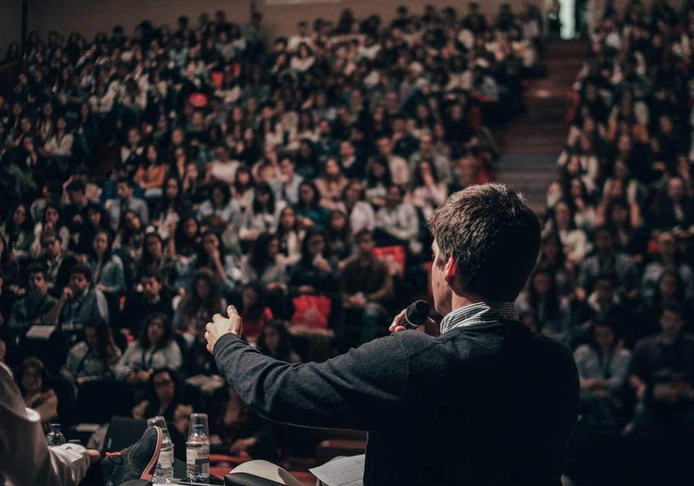 Man speaking to large crowd confidently after receiving presentation coaching from Chris Zervas